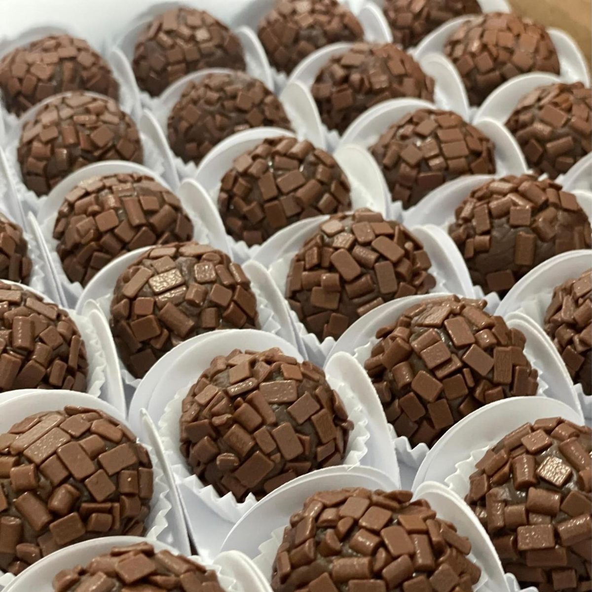 Brigadeiros tradicionais cobertos com placas de chocolate, em forminhas brancas
